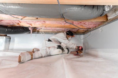 Groundworks worker installing a vapor barrier in a crawl space.