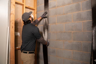 man in hat installing carbon fiber reinforcement on a cement block basement wall