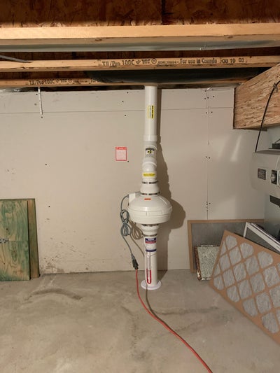 A radon mitigation system installed under the stairs of a home