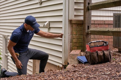 AquaGuard man inspecting downspout near a home's foundation.