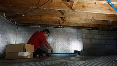 Man in crawl space installing insulation.