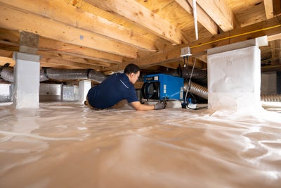 A Groundworks employee performing maintenance in a crawl space