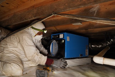 employee setting up a dehumidifier inside a crawl space
