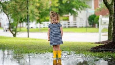 sad little girl standing in front of puddle in yard