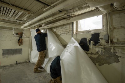 A worker installing a basement wall vapor barrier in a basement.