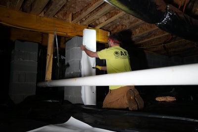 AFS crewman attaching vapor barrier to a support column in crawl space.