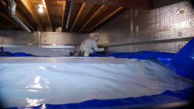 technician installing crawl space insulation and vapor barrier