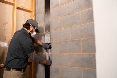 Crewman installing carbon fiber straps on a block wall.
