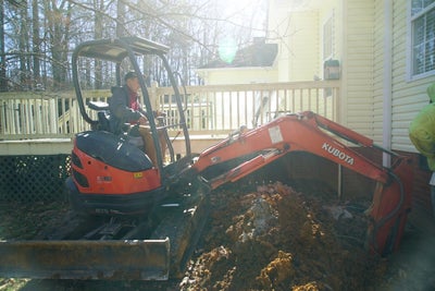 Excavator machine being used to clear soil from around a foundation.