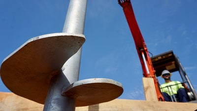 closeup of helical pier with crew member and heavy machinery
