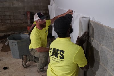 Two AFS installers placing vapor barrier onto basement wall.
