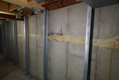 Three steel I-beams on a concrete basement wall.