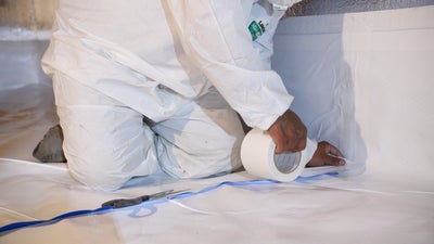 crew member taping a crawl space vapor barrier into place
