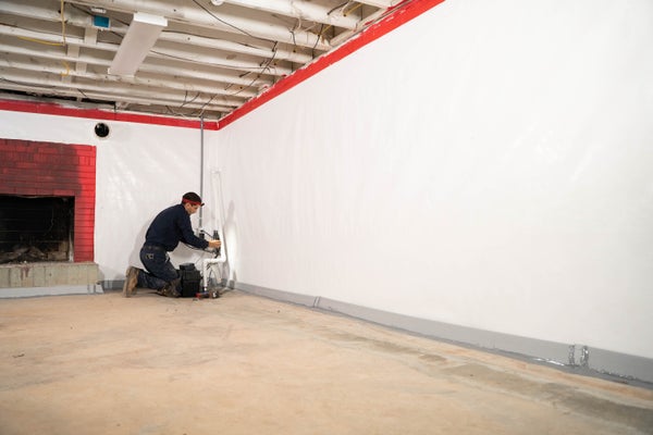 Man installing a vapor barrier for basement waterproofing purposes.