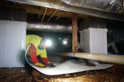 Man installing a vapor barrier inside a crawl space.