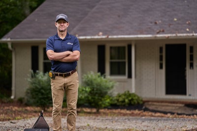 AquaGuard inspector posing in front of home with arms crossed.