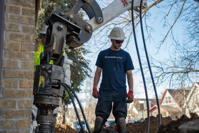 A groundworks employee installing a foundation pier for these homeowners