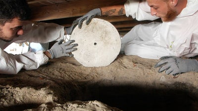 two crew members in crawl space with concrete footing wheel
