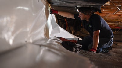 Alpha Foundations installer placing a vapor barrier along the walls of a crawl space.