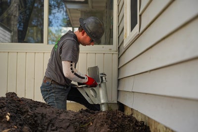 Alpha Foundations installer placing a foundation pier into soil next to wall.
