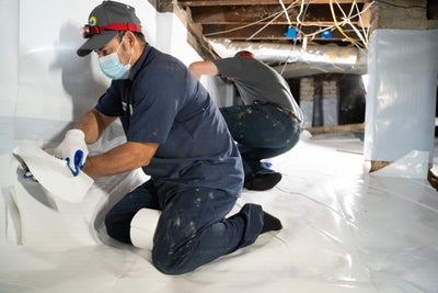 A Groundworks worker installing a vapor barrier in a crawl space.