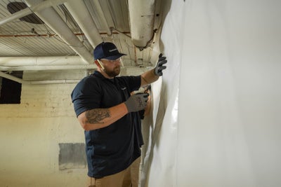 Crewman installing a basement wall vapor barrier.