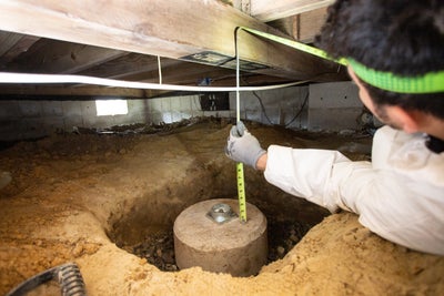 Technician measuring the height of a pier and beam foundation.