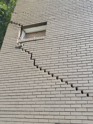 A large crack on the exterior of a wall of a residential home.