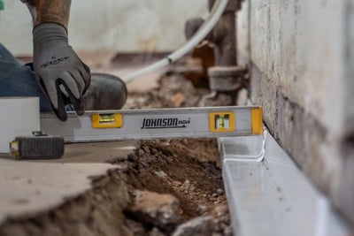 Close up of a worker using a level to ensure a basement is getting adequate drainage.