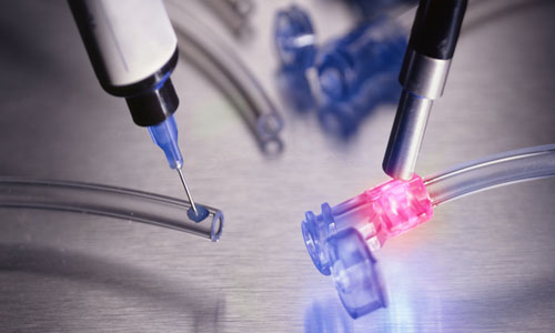 A Dymax adhesive with See-Cure and Ultra-Red fluorescing is dispensed onto a tube set and then cured with a spot curing light guide.