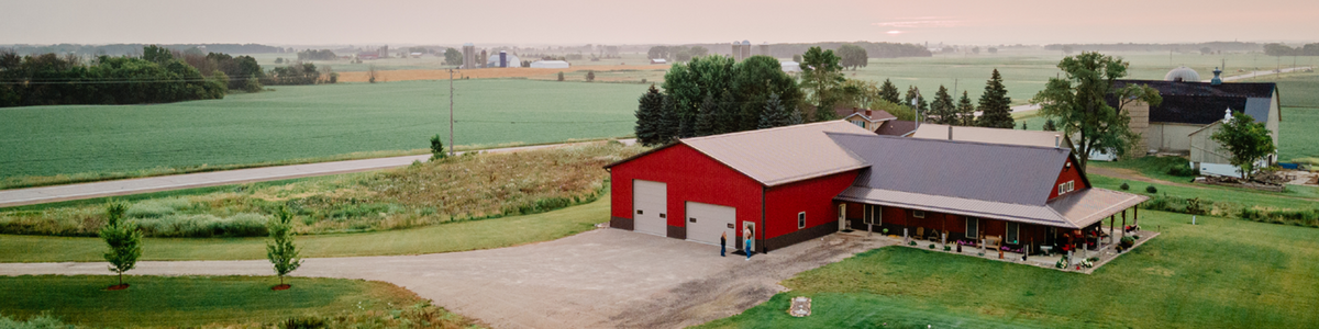 A red barn and house sit on a sprawling green farm property.