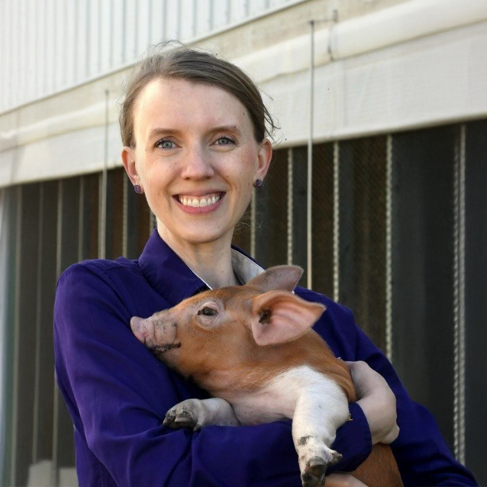 Dr. Megan Roberts smiles while holding a piglet.