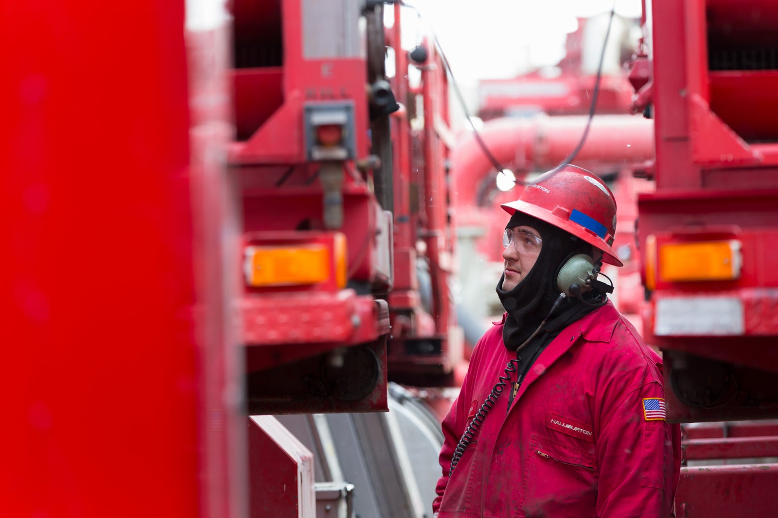 Halliburton employee in red coveralls next to hydraulic fracturing trucks.