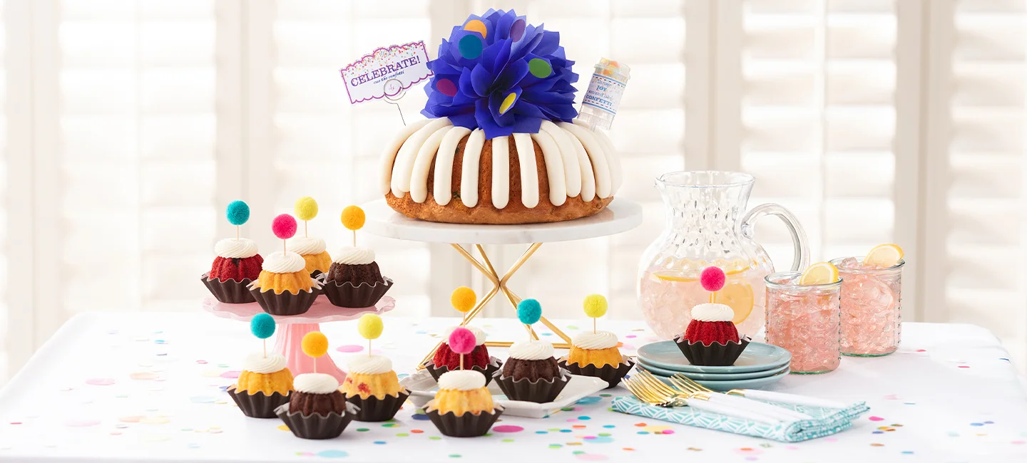 A Bundt Cake topped with a navy bow and a Celebrate flag, along with Bundtinis® decorated with pom-pom toppers.