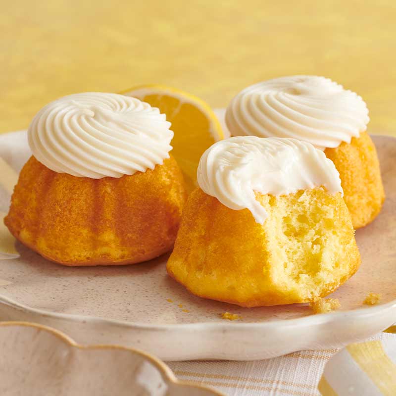 Assorted flavors of mini Bundt cakes crowned with cream cheese sitting on a plate - Shop Bundtinis