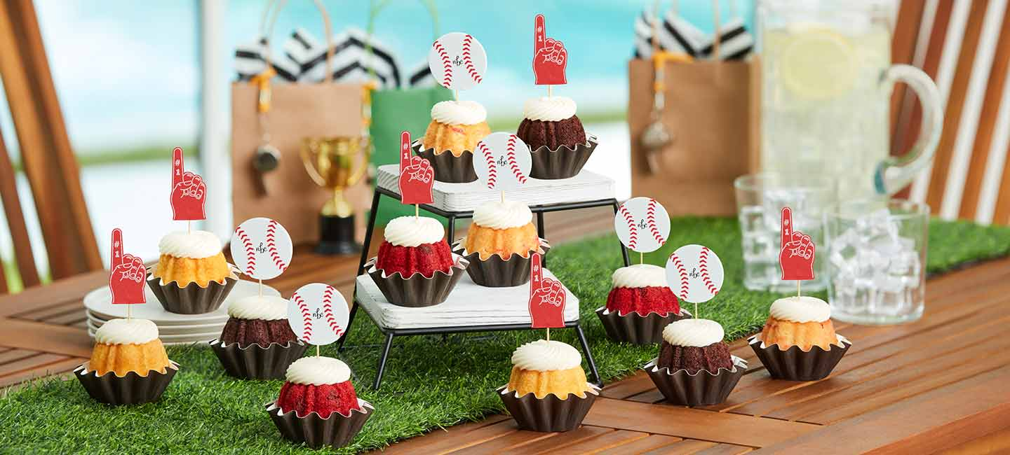Mini Bundt cakes topped with cream cheese frosting and basketball and foam finger decorations, arranged on a sports themed dessert table for a game day celebration.