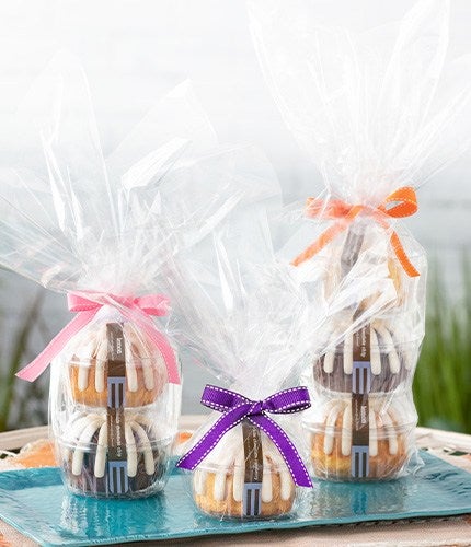 Three gift wrapped stacks of mini bundt cakes, each packaged in clear cellophane and tied with colorful ribbons pink, purple, and orange, displayed on a turquoise tray.