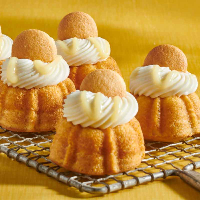 Assorted flavors of mini Bundt cakes crowned with cream cheese sitting on a plate - Shop Bundtinis