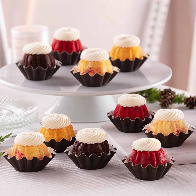 Assorted flavors of mini Bundt cakes crowned with cream cheese sitting on a plate - Shop Bundtinis