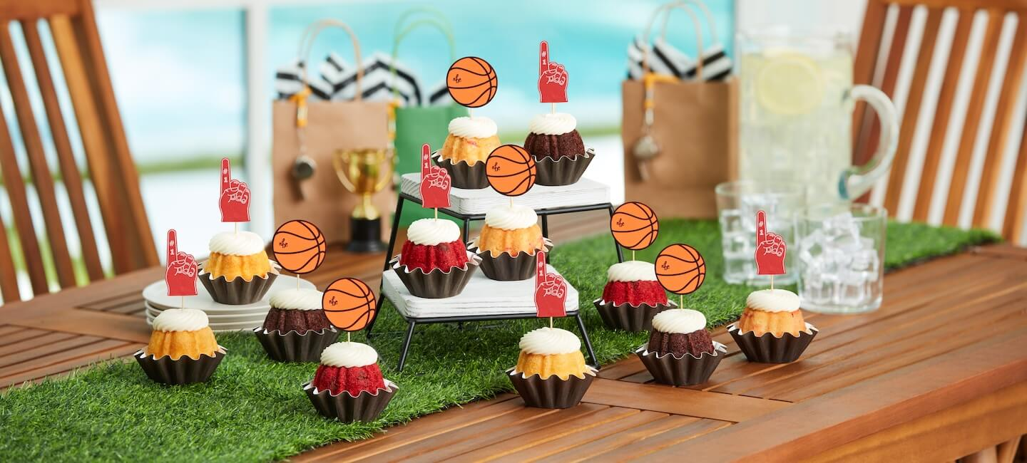 Mini Bundt cakes topped with cream cheese frosting and basketball and foam finger decorations, arranged on a sports themed dessert table for a game day celebration.