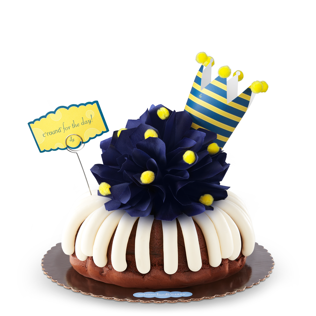 A bundt cake with a navy colored bow with golden pom-poms. A nay and yellow crown tops the cake along with card that says c'round' for the day!.