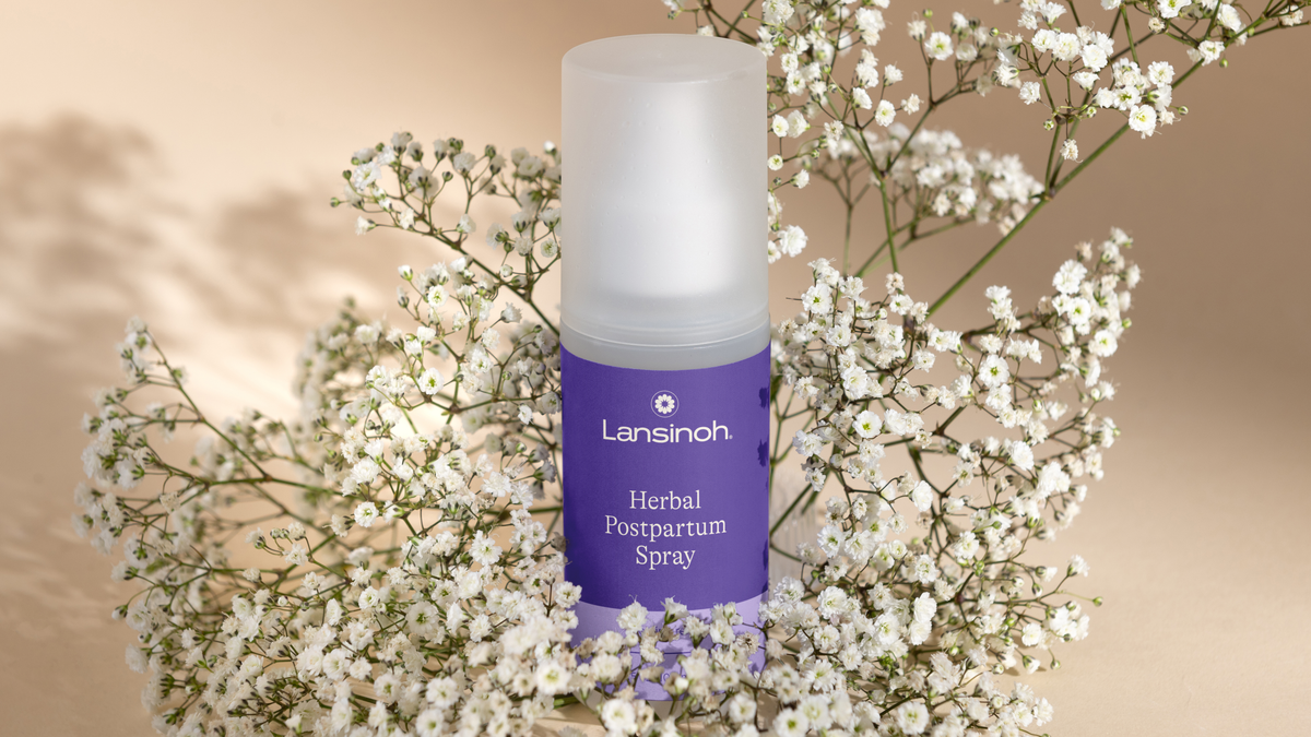 Herbal postpartum spray bottle surrounded by delicate white flowers on a beige background.