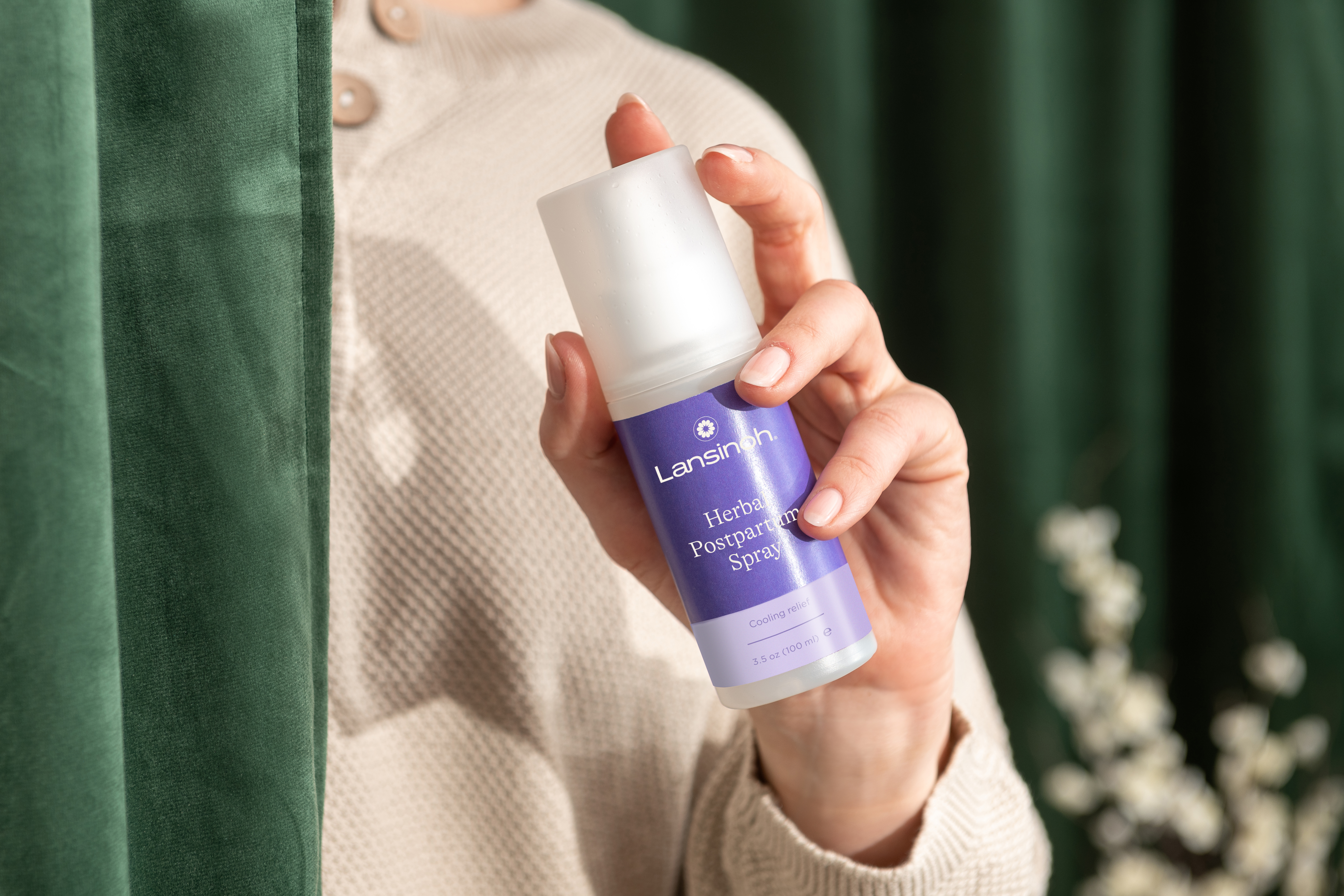 Person holding a bottle of Lansinoh herbal postpartum spray.