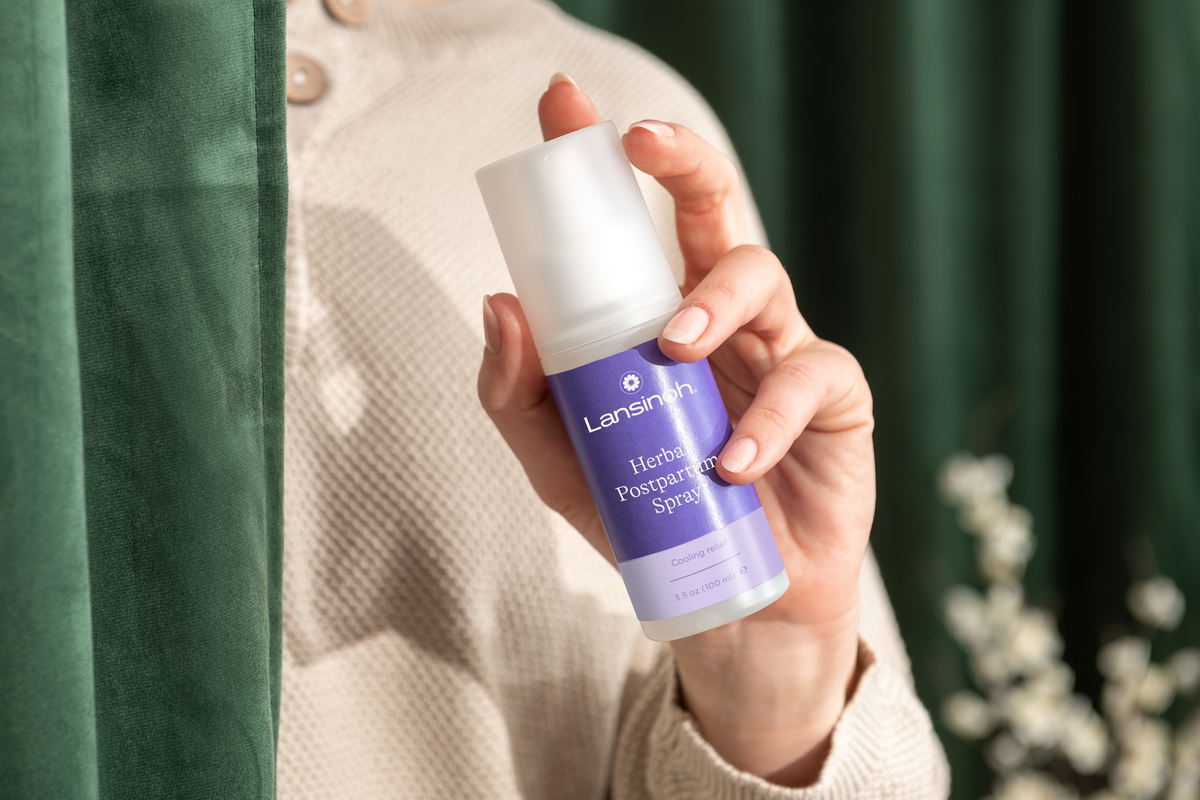 Person holding a bottle of Lansinoh herbal postpartum spray.