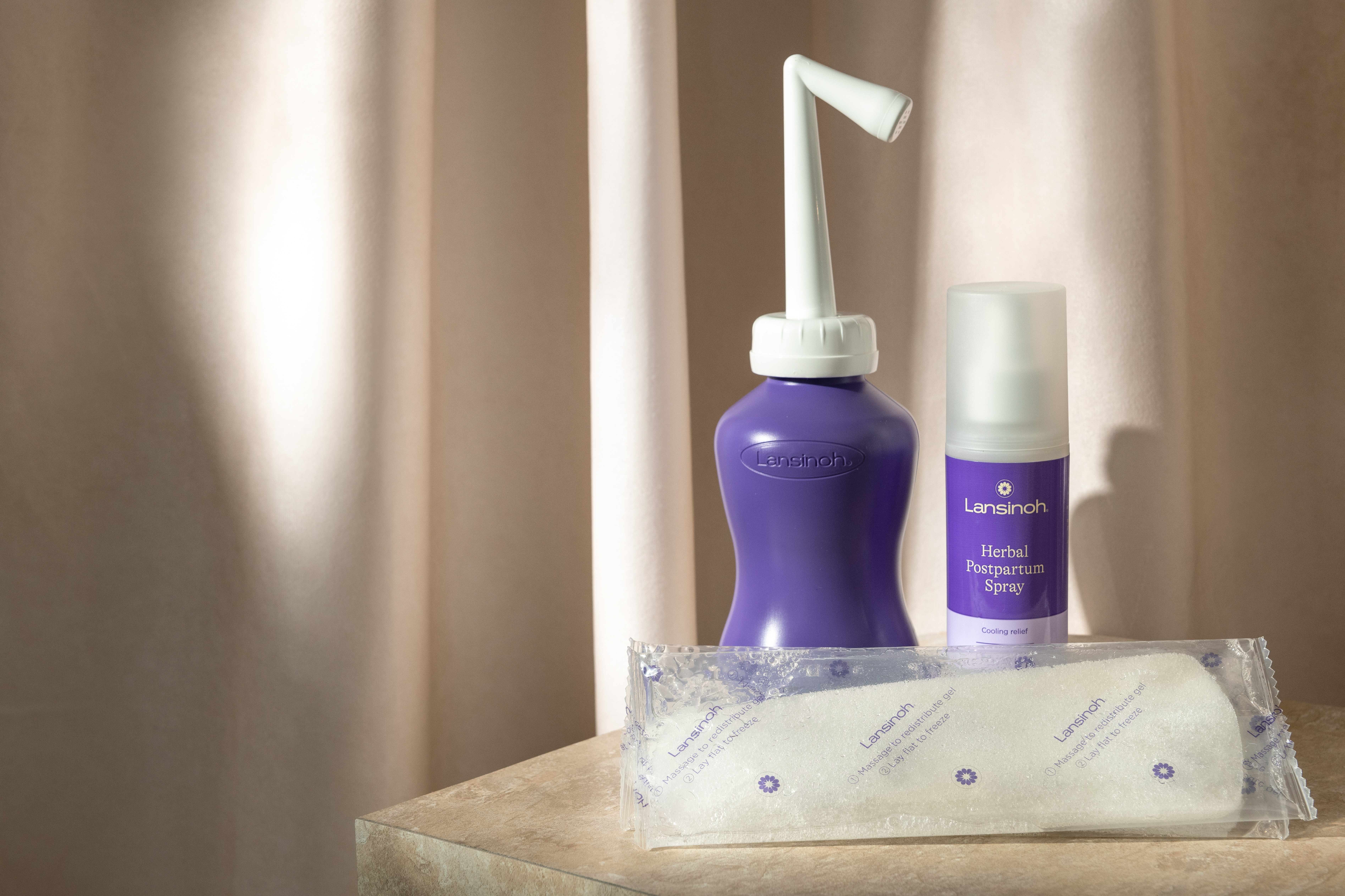 Lansinoh breastfeeding products displayed on a countertop with a draped beige backdrop.