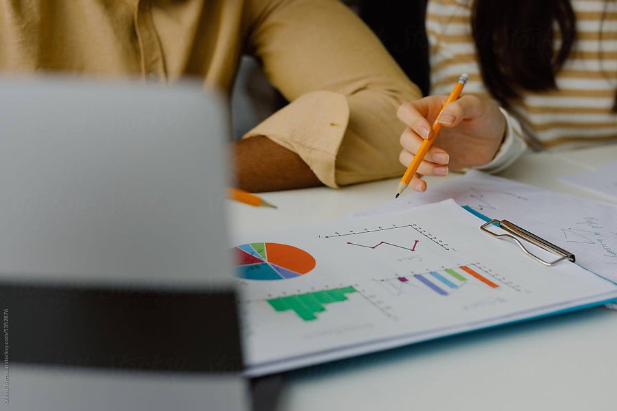 Two women discussing charts and graphs on paper at a table.