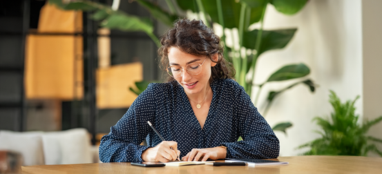 A woman is sitting at a table writing in a notebook