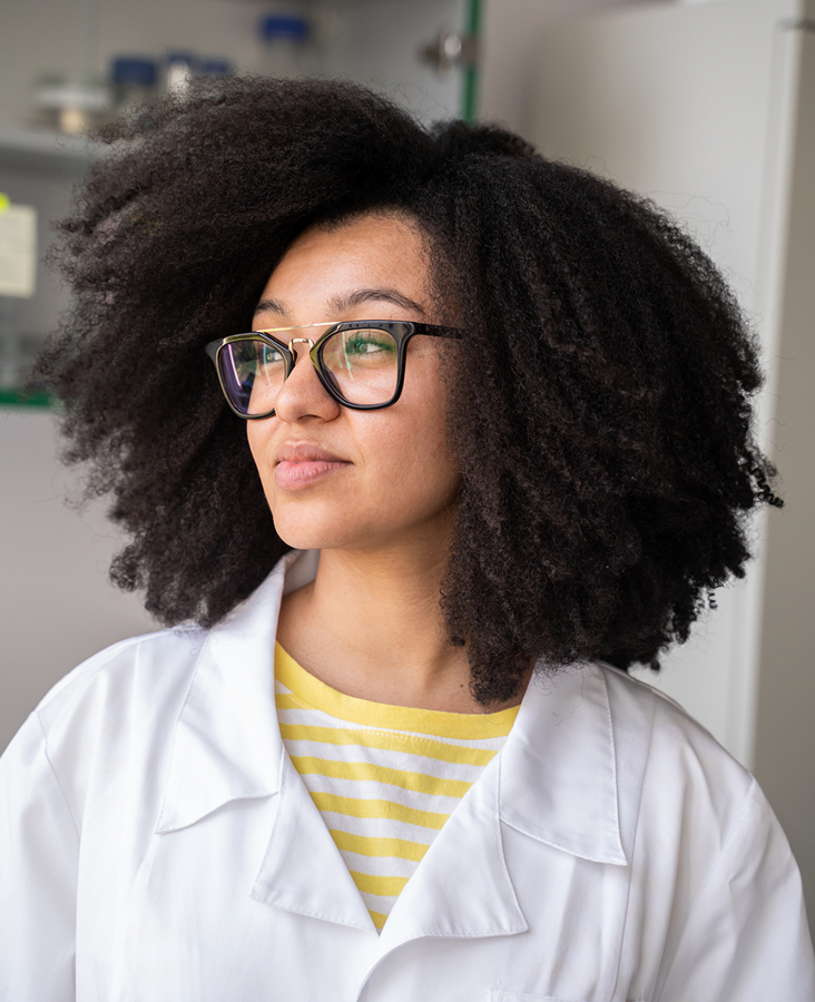 A female scientist with curly hair in a white lab coat and glasses.
