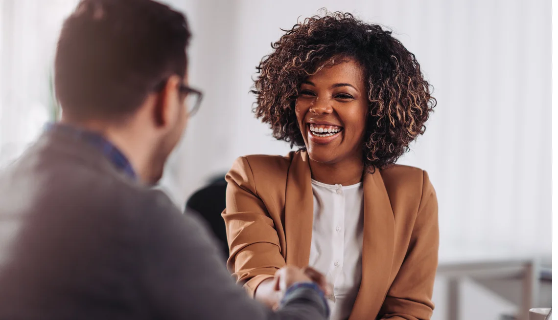 Two office workers shaking hands while at a meeting table.