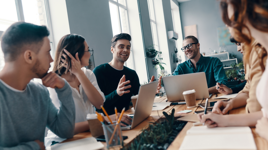 A group of people are sitting around a table with laptops